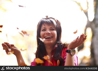 Beautiful girl with falling leaves in the autumn park