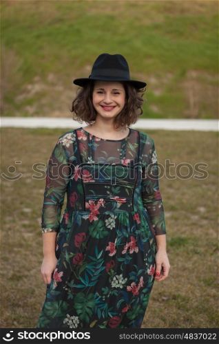 Beautiful girl with flowered dress an black hat in the landscape