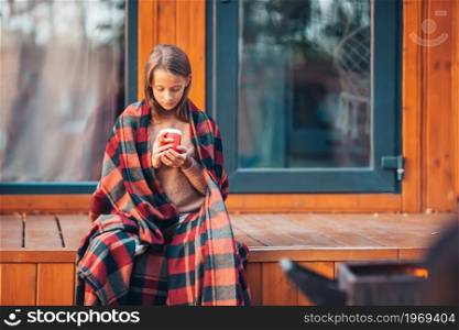 Beautiful girl with hot cacao enjoying autumn day on the terrace. Beautiful girl wrapped in a blanket at autumn warm day