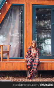 Beautiful girl with hot cacao enjoying autumn day on the terrace. Beautiful girl wrapped in a blanket at autumn warm day