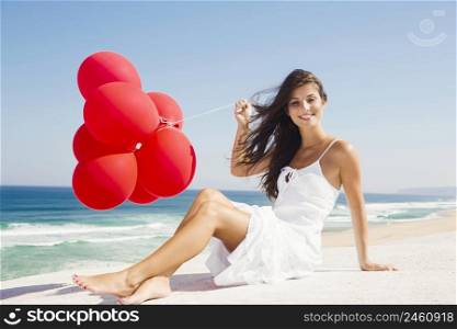 Beautiful girl with red ballons sitting in the beach