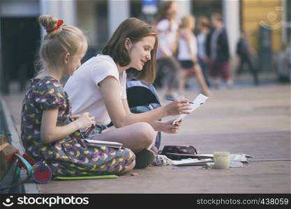 Beautiful girls sit and paint on the square.