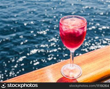 Beautiful glass of pink wine on the open deck of a cruise liner against the backdrop of blue sea waves. Side view, close-up. Concept of leisure and travel. Man holding a beautiful glass of pink wine