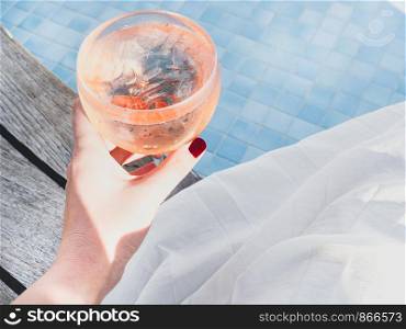 Beautiful glass with a pink cocktail and ice cubes on the background of the pool with blue water. Top view, close-up. Rest during a sea cruise. Beautiful glass with a pink cocktail and ice cubes