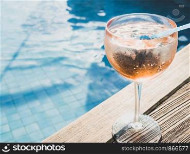 Beautiful glass with a pink cocktail and ice cubes on the background of the pool with blue water. Top view, close-up. Rest during a sea cruise. Beautiful glass with a pink cocktail and ice cubes