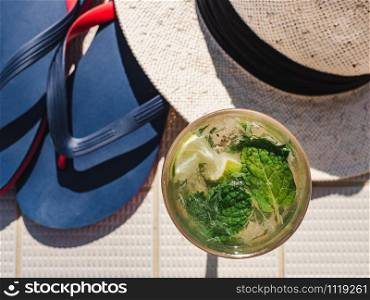 Beautiful glass with refreshing mojito and ice cubes on the background of the plank deck. Top view, close-up. Concept of leisure and travel. Beautiful glass with refreshing mojito and ice cubes