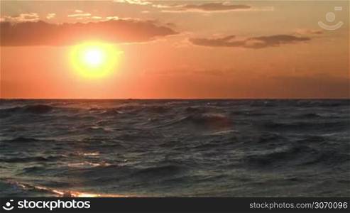 Beautiful golden sunset over sea with strong waves. Rough water in the evening sunlight