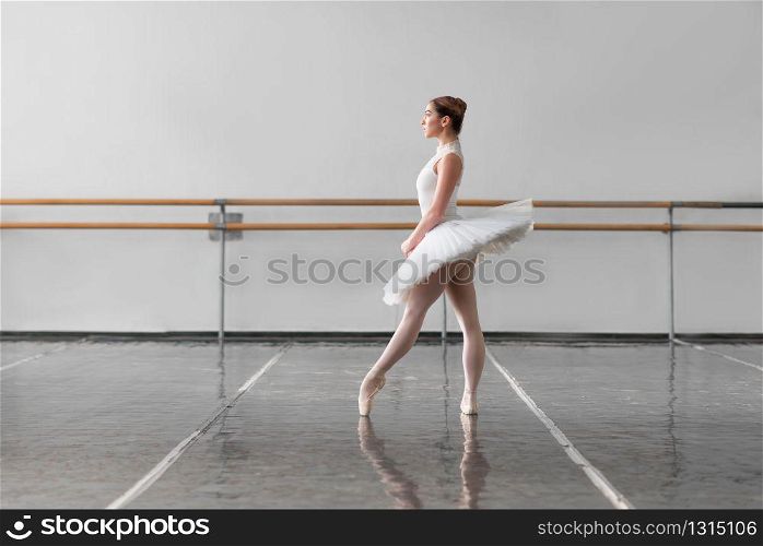 Beautiful grace ballerina keep the rack in ballet class, bars and white wall on background