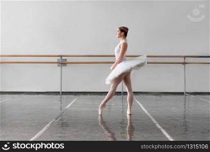 Beautiful grace ballerina keep the rack in ballet class, bars and white wall on background