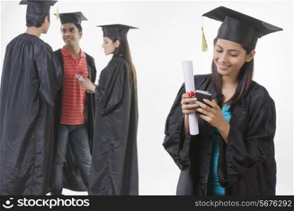Beautiful graduate student using mobile phone with friends discussing over white background