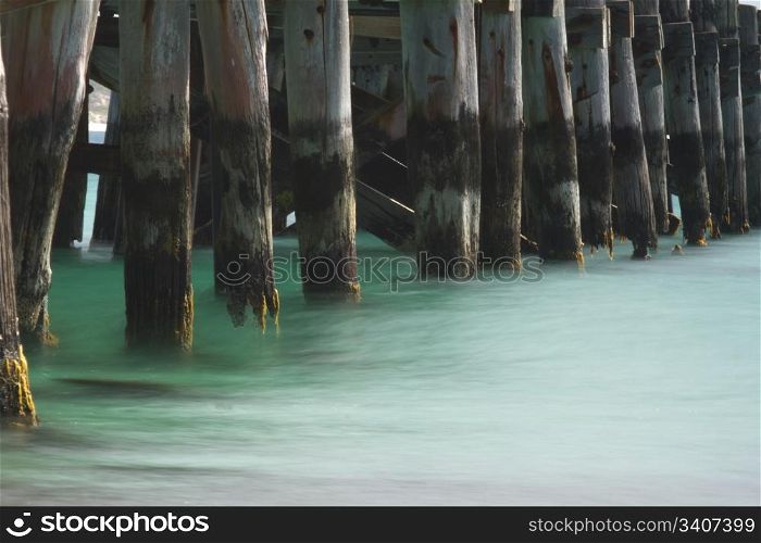 Beautiful green of a silky, low tide sweeps beneath the timbers of an ocean pier. Location is Vivonne Bay, Kangaroo Island, Australia.
