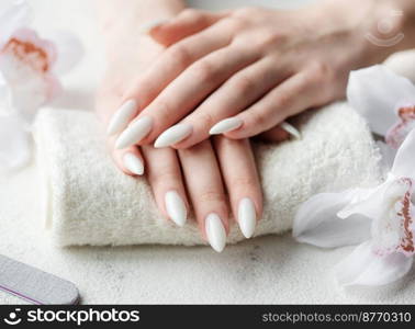 Beautiful hands of a young woman with white manicure on nails. Female hands on a towel in a nail salon and white orchids flowers