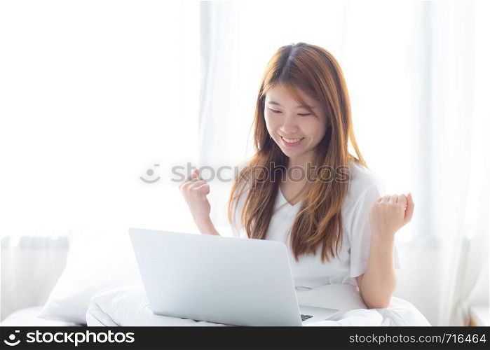 Beautiful happiness young asian woman using laptop work with success on bed in the home, girl and notebook shopping online with glad, communication concept.