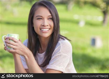 Beautiful happy Asian Eurasian young woman or girl outside drinking mug of tea or coffee