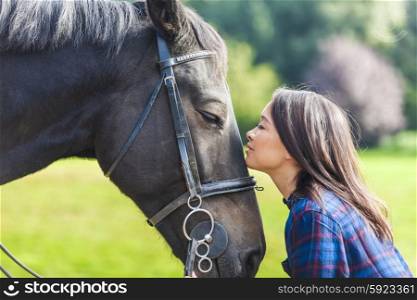 Beautiful happy Asian Eurasian young woman or girl wearing plaid checked shirt, smiling and resting her head on her horse in sunshine