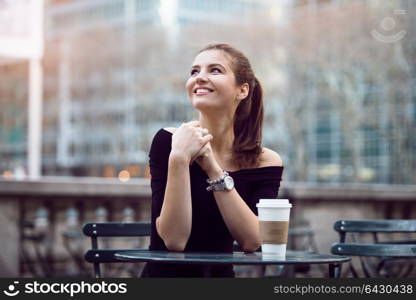 Beautiful happy businesswoman sitting in city park during lunch time or coffee break with paper coffee cup. Woman with coffee smiling outdoors.