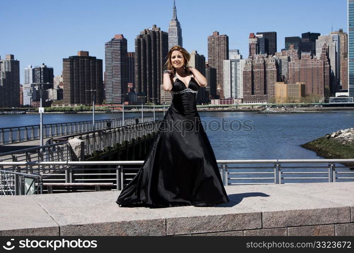 Beautiful happy Caucasian Latina fashion model woman in black evening cocktail dress posing standing in front of skyline of Manhattan, New York City.