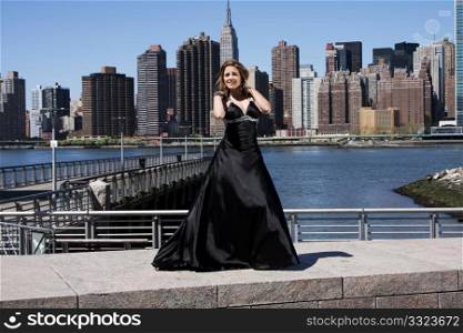 Beautiful happy Caucasian Latina fashion model woman in black evening cocktail dress posing standing in front of skyline of Manhattan, New York City.