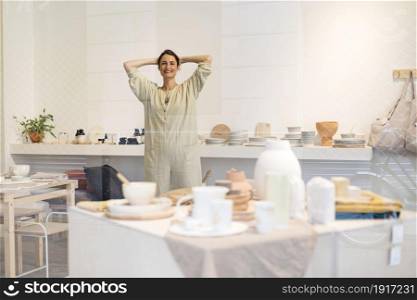 Beautiful happy craft woman wearing apron looking at camera and smiling while standing in her art studio or craft pottery shop. Portrait of beautiful happy craft woman wearing apron and smiling while standing in her art studio or craft pottery shop