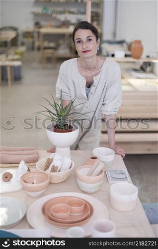 Beautiful happy craft woman wearing apron looking at camera and smiling while standing in her art studio