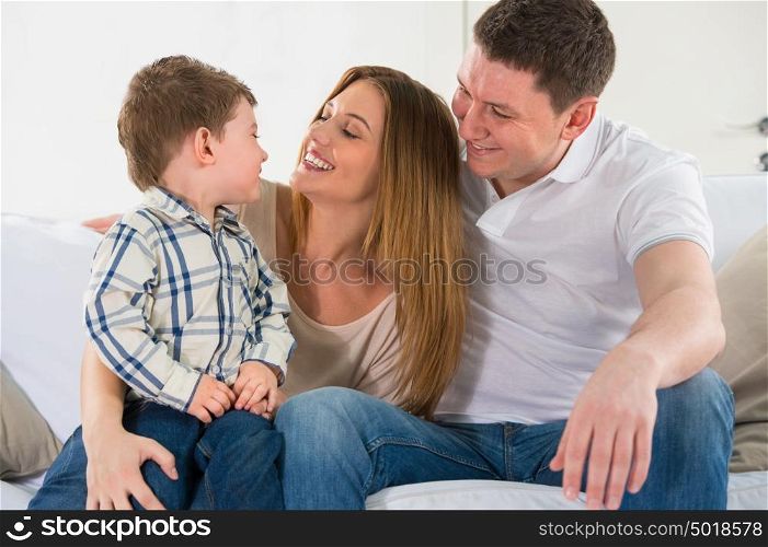 Beautiful happy family having fun at home - parents playing with their son on sofa