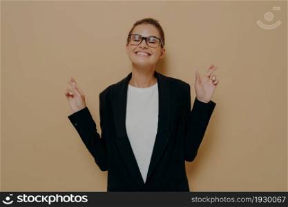 Beautiful happy female keeping her fingers crossed and eyes closed to make desired wish, asking for good luck before important event while posing isolated over studio background. Body language concept. Beautiful happy female keeping her fingers crossed and eyes closed to make desired wish