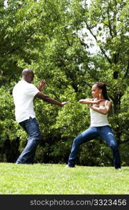 Beautiful happy fun young African American couple, together exercising martial arts in a park.
