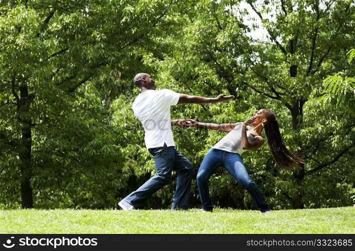 Beautiful happy fun young African American couple, together exercising martial arts in a park