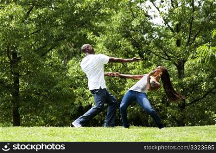 Beautiful happy fun young African American couple, together exercising martial arts in a park