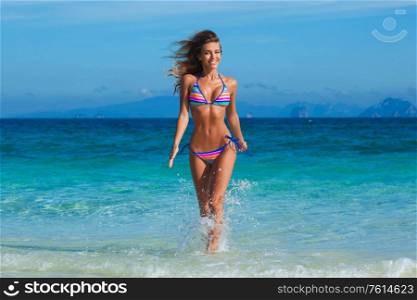 Beautiful happy girl in bikini running in tropical sea waves. Girl running in sea waves