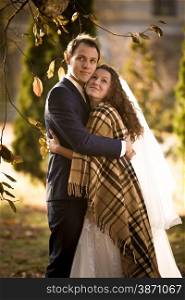 Beautiful happy just married couple covering with plaid at autumn park