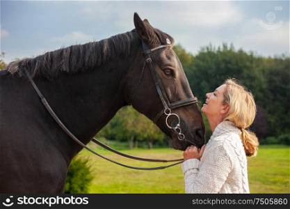Beautiful happy middle aged woman laughing, smiling and holding her horse close in sunshine