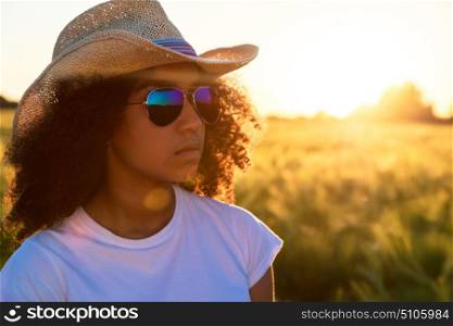 Beautiful happy mixed race African American female girl teenager young woman wearing relective aviator sunglasses and cowboy hat in a cornfield at golden sunset or sunrise