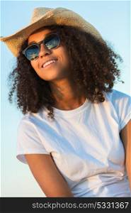 Beautiful happy mixed race African American female girl teenager young woman wearing relective aviator sunglasses and cowboy hat outside at golden sunset or sunrise
