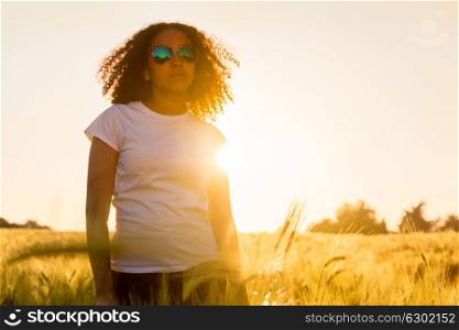 Beautiful happy mixed race African American female girl teenager young woman wearing relective aviator sunglasses in a cornfield at golden sunset or sunrise
