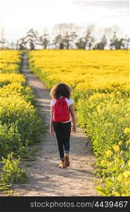 Beautiful happy mixed race African American girl teenager female young woman hiking with red recksack in yellow field in golden evening sunshine
