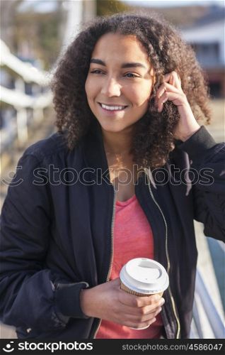 Beautiful happy mixed race African American girl teenager female young woman smiling drinking takeaway coffee outside wearing black bomber jacket