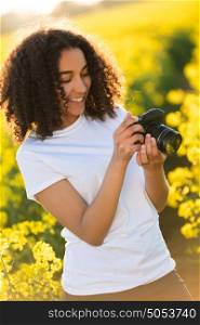 Beautiful happy mixed race African American girl teenager female young woman smiling outdoors in sunshine taking photographs with a camera