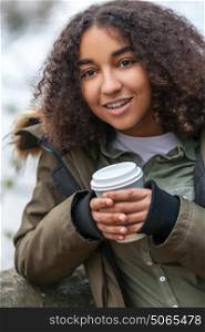 Beautiful happy mixed race African American girl teenager female young woman smiling drinking takeaway coffee outside in winter