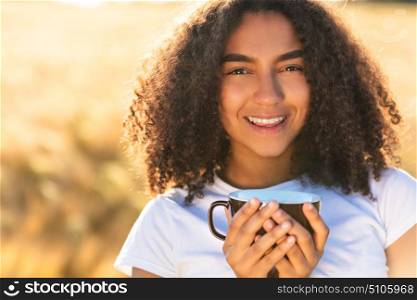 Beautiful happy mixed race African American girl teenager female young woman smiling with perfect teeth white,drinking coffee or tea outdoors