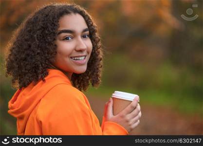 Beautiful happy mixed race African American girl teenager female young woman smiling with perfect white teeth,drinking coffee or tea outdoors in Fall or Autumn