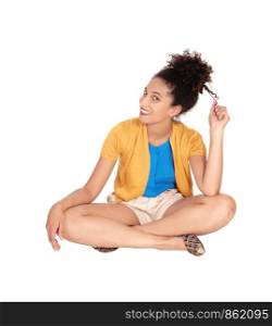 Beautiful happy multi-racial woman sitting on the floor playing with her hair in shorts and a yellow sweater with her curly black hair and smilingisolated for white background