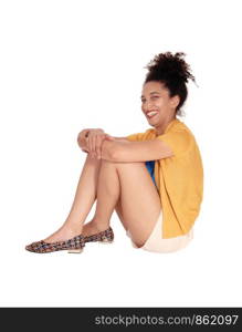 Beautiful happy multi-racial woman sitting on the floor with her arms around her knees in shorts and a yellow sweater with her curly black hair isolated for white background