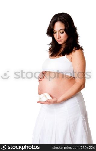 Beautiful happy pregnant woman dressed in white holding a pair of yellow baby shoes next to her bare belly, isolated