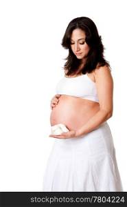 Beautiful happy pregnant woman dressed in white holding a pair of yellow baby shoes next to her bare belly, isolated