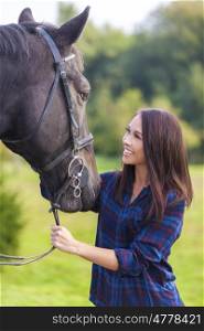 Beautiful happy smiling Asian Eurasian young woman or girl wearing plaid checked shirt with her her horse in sunshine