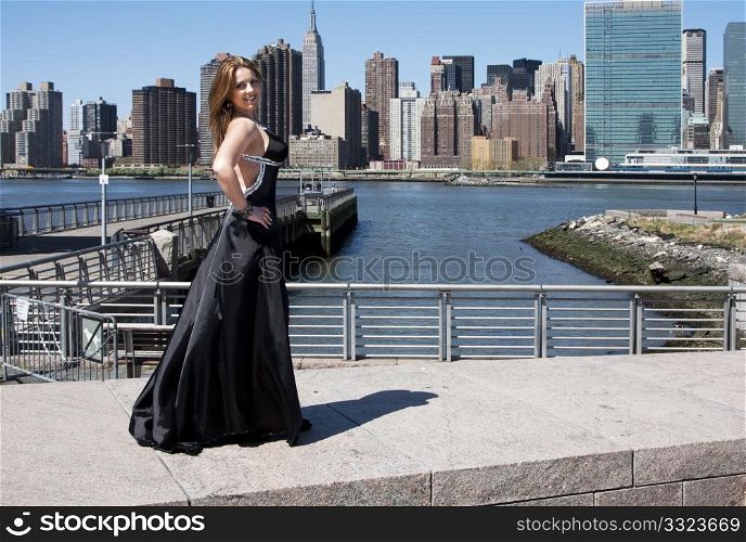Beautiful happy smiling Caucasian Latina fashion model woman in black evening cocktail dress posing standing in front of skyline of Manhattan, New York City.
