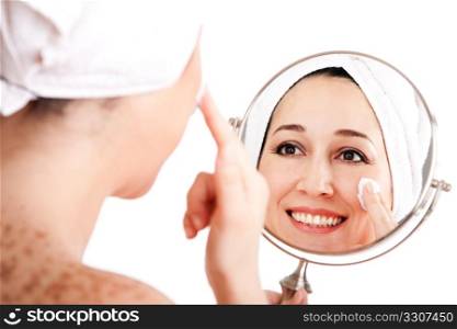 Beautiful happy smiling woman face applying exfoliating cream as anti-aging skincare treatment while looking at mirror, isolated.