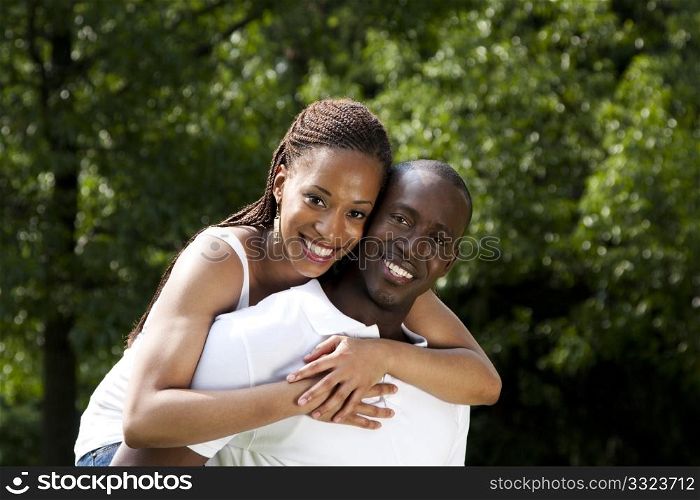 Beautiful happy smiling young African American couple in love wearing white shirts, woman hugging man, with trees in the background.