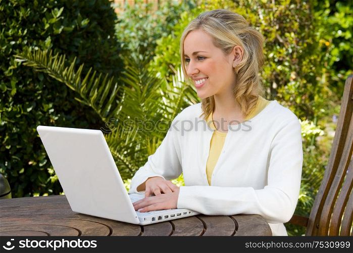 Beautiful happy smiling young woman teenage girl using a white laptop computer in her garden at home